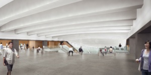 A spacious, modern interior with a bright ceiling featuring angled beams. People are walking and sitting around, with a glass railing and stairs leading to a lower level. The atmosphere is open and airy.