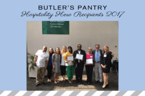 Group of people standing indoors, smiling, and holding certificates. They are part of the "Butler's Pantry Hospitality Hero Recipients 2017." A sign in the background mentions a ballroom and conference location.