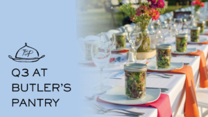 A long, elegantly set table outdoors with colorful flower arrangements and jars filled with salad as placeholders. The left side features text reading "Q3 at Butler's Pantry" with a logo above.
