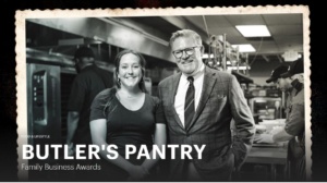 A black and white photo showing a man in a suit and a woman in a T-shirt smiling in a kitchen setting. They are surrounded by people working. Text reads: "Butler's Pantry Family Business Awards.