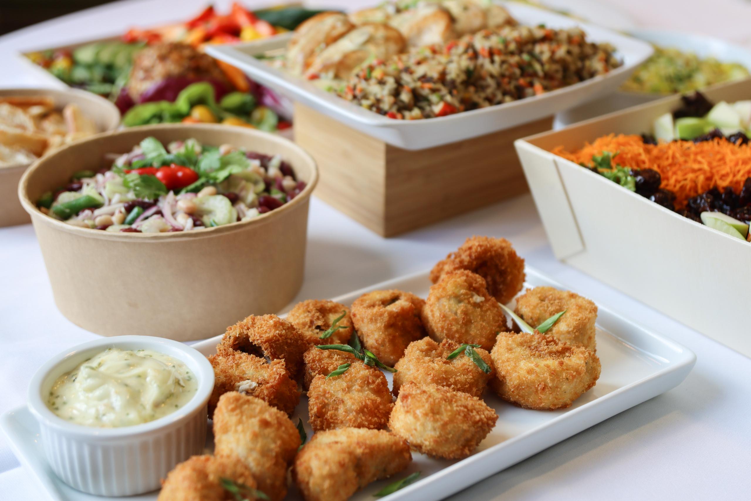 A table with assorted salads, fried appetizers, rice, and a bowl of dipping sauce.